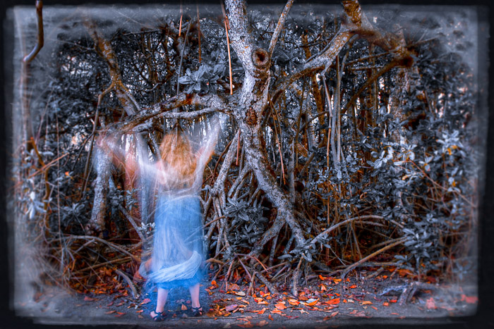 Blurred figure in a blue dress with raised arms among mangrove roots