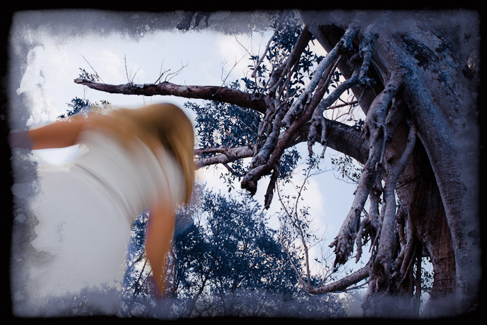 Blurred figure leaning beneath a tree with exposed mangrove branches