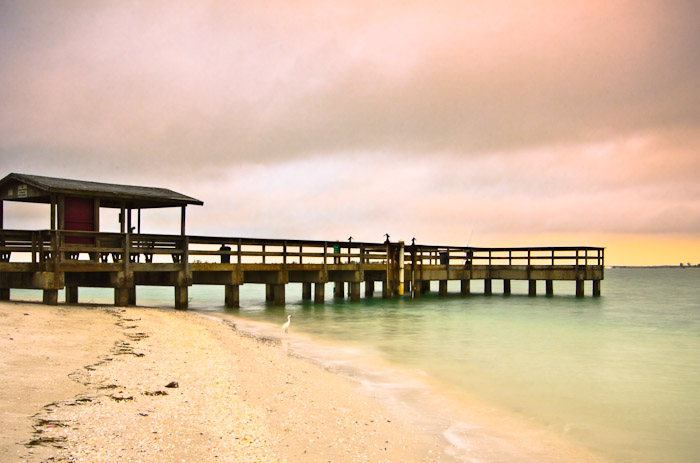 Pier extending over calm water beneath a pink sky